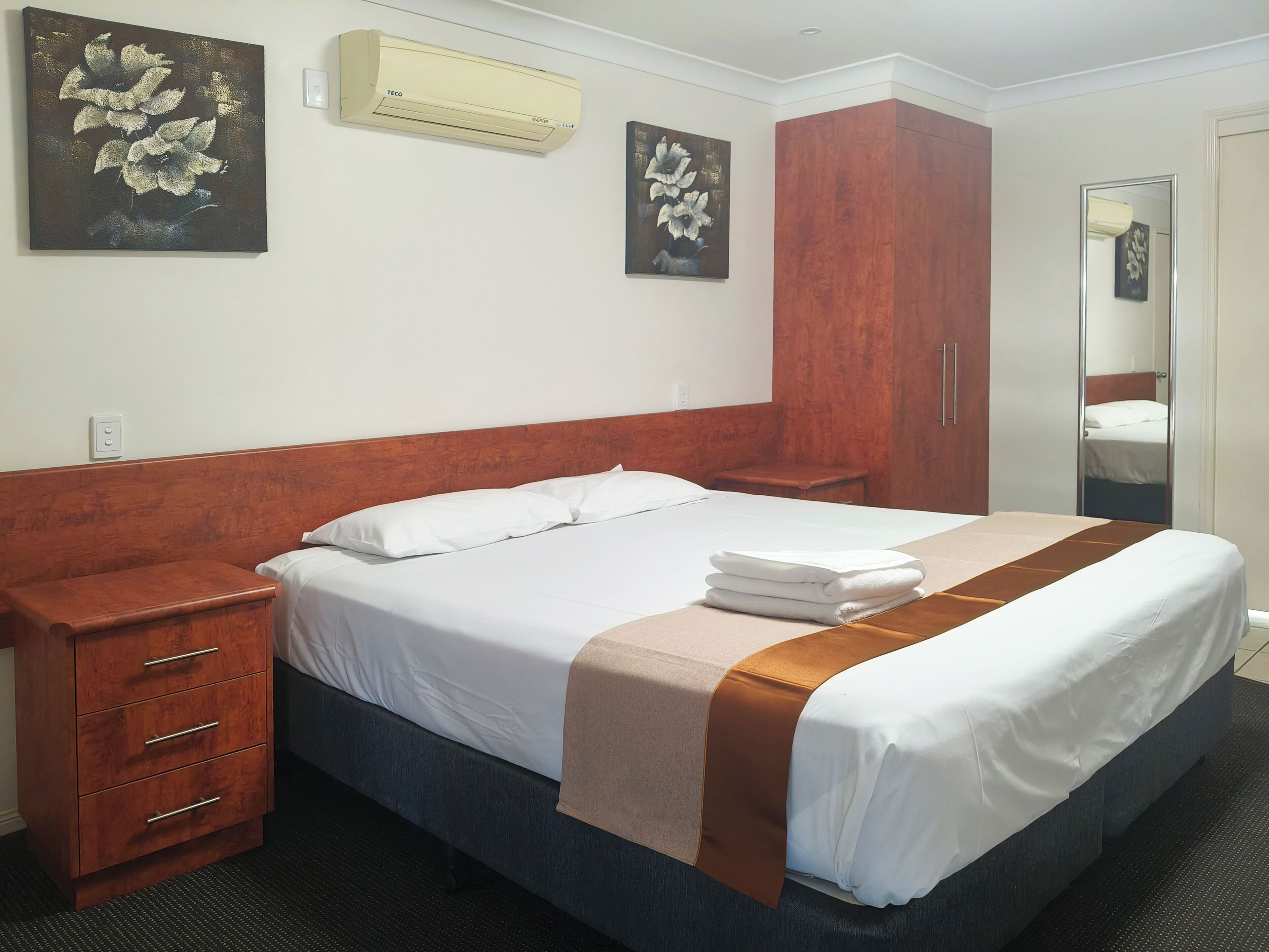 Habitación de hotel con cama, mesita de noche de madera, armario y dos unidades de aire acondicionado fijadas a la pared.