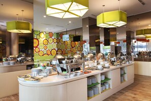 Un buffet avec différents stands de nourriture, un mur décoré d’un motif de fruits et des suspensions lumineuses jaunes vives.