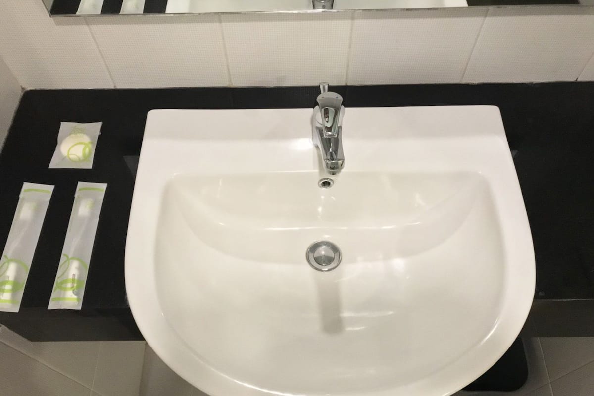 Un évier blanc avec un robinet chromé, un plan de travail noir et un miroir au-dessus.