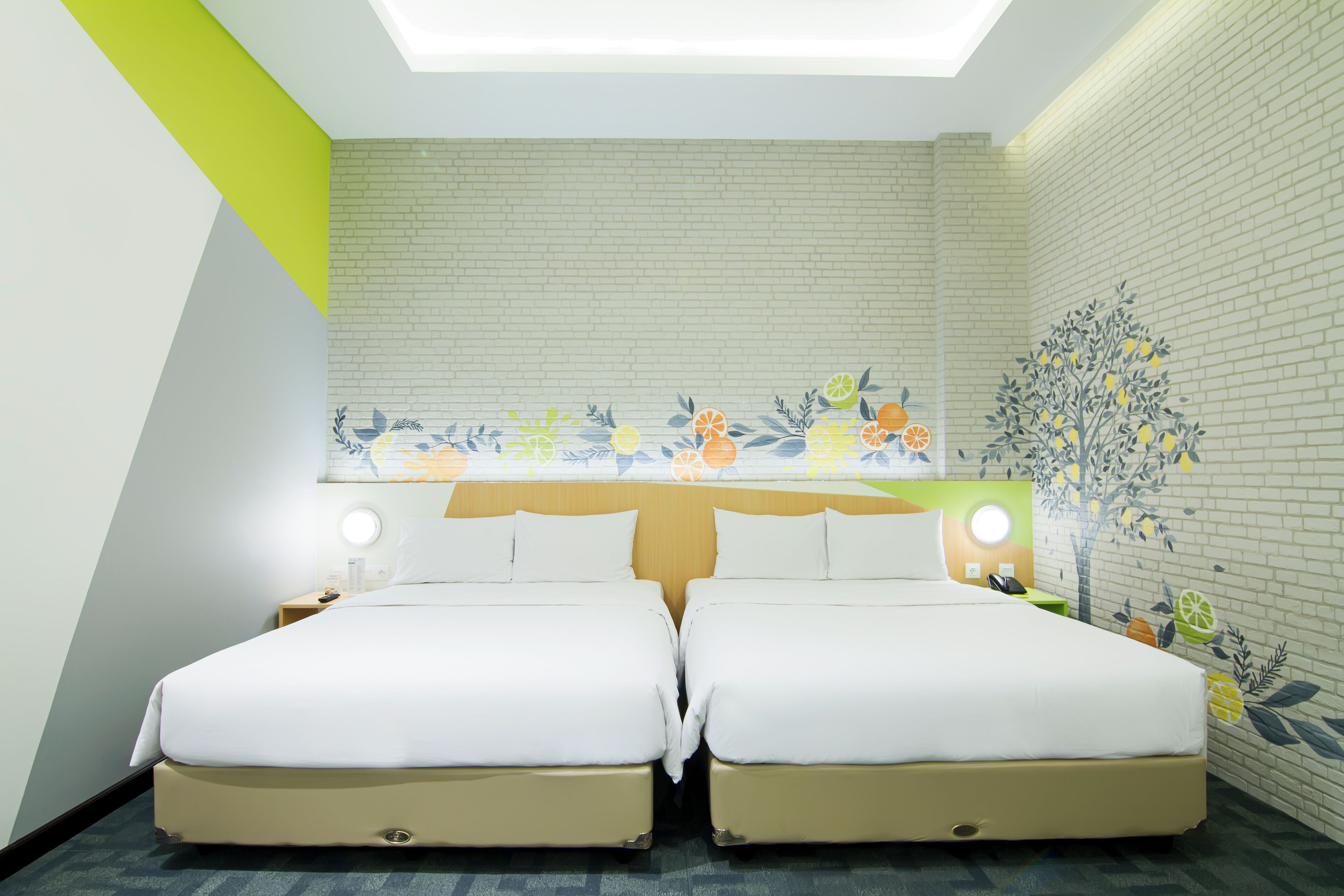 A hotel room with two beds, a skylight, a brick wall, and a floral mural.