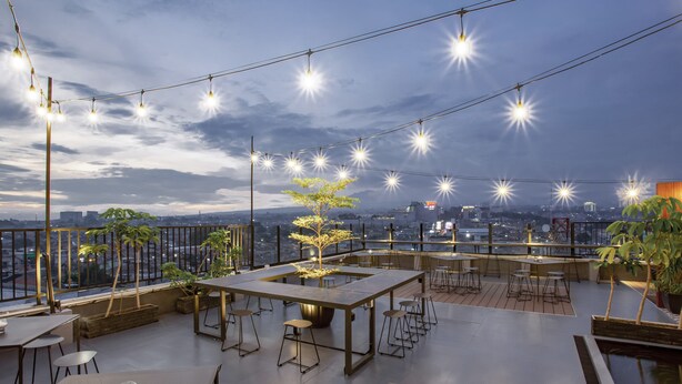 Een dakterras met tafels en stoelen, lichtjes en uitzicht op de stadsgezicht.