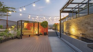 Een terras op het dak met lichtslingers, een houten bank, een bakstenen muur en een waterpartij.