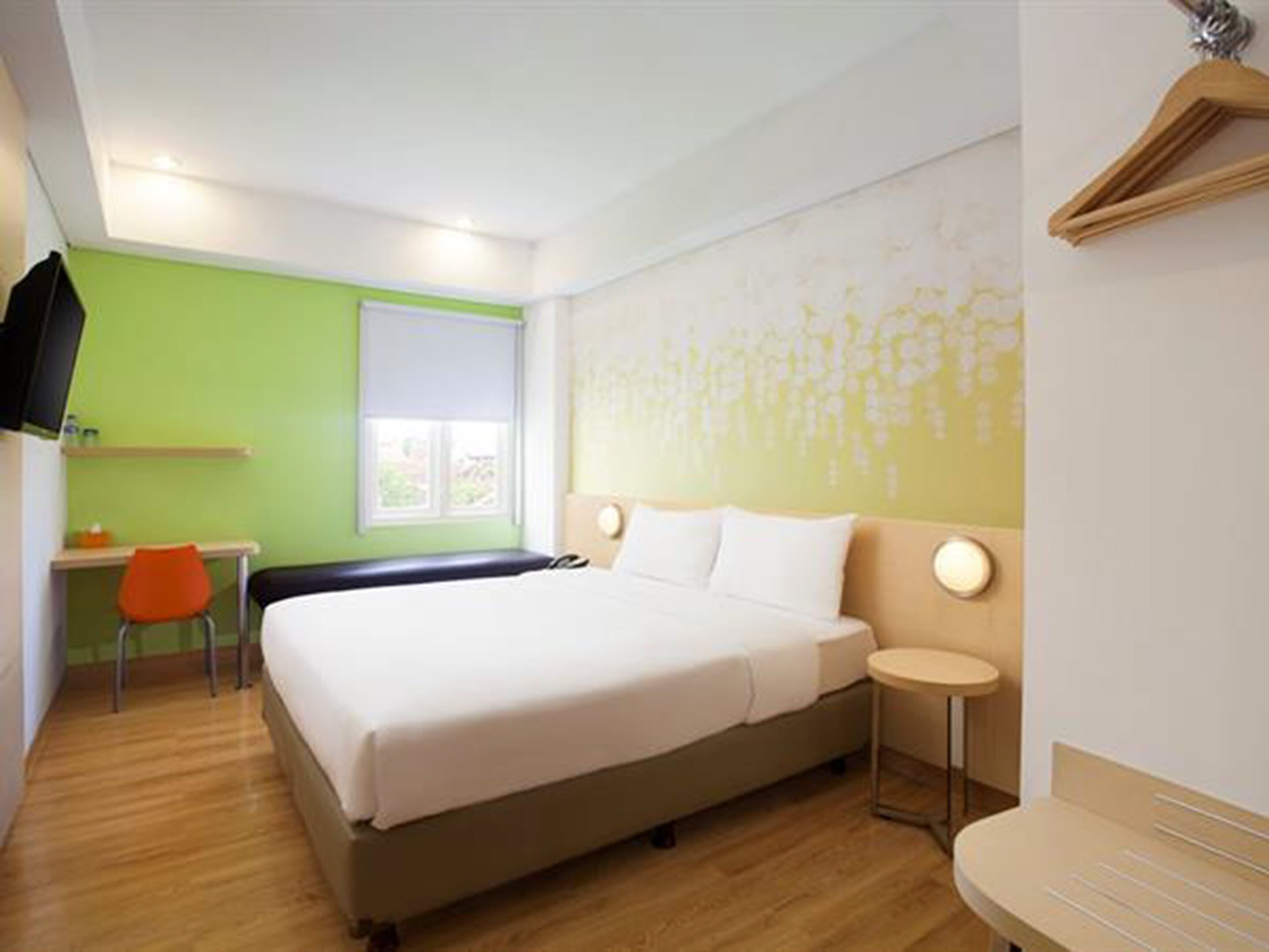 A hotel room with a bed, a desk, a chair, and a small table.