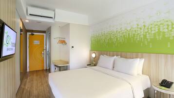 A hotel room with a large bed, a bedside table, a wall-mounted TV, and a green floral wall design.