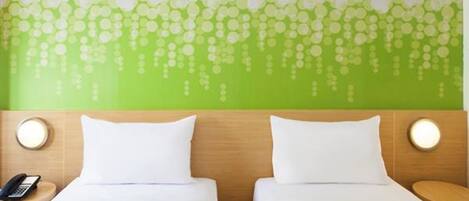 Una habitación de hotel con dos camas, una pared verde con diseño de hojas y lámparas de noche.
