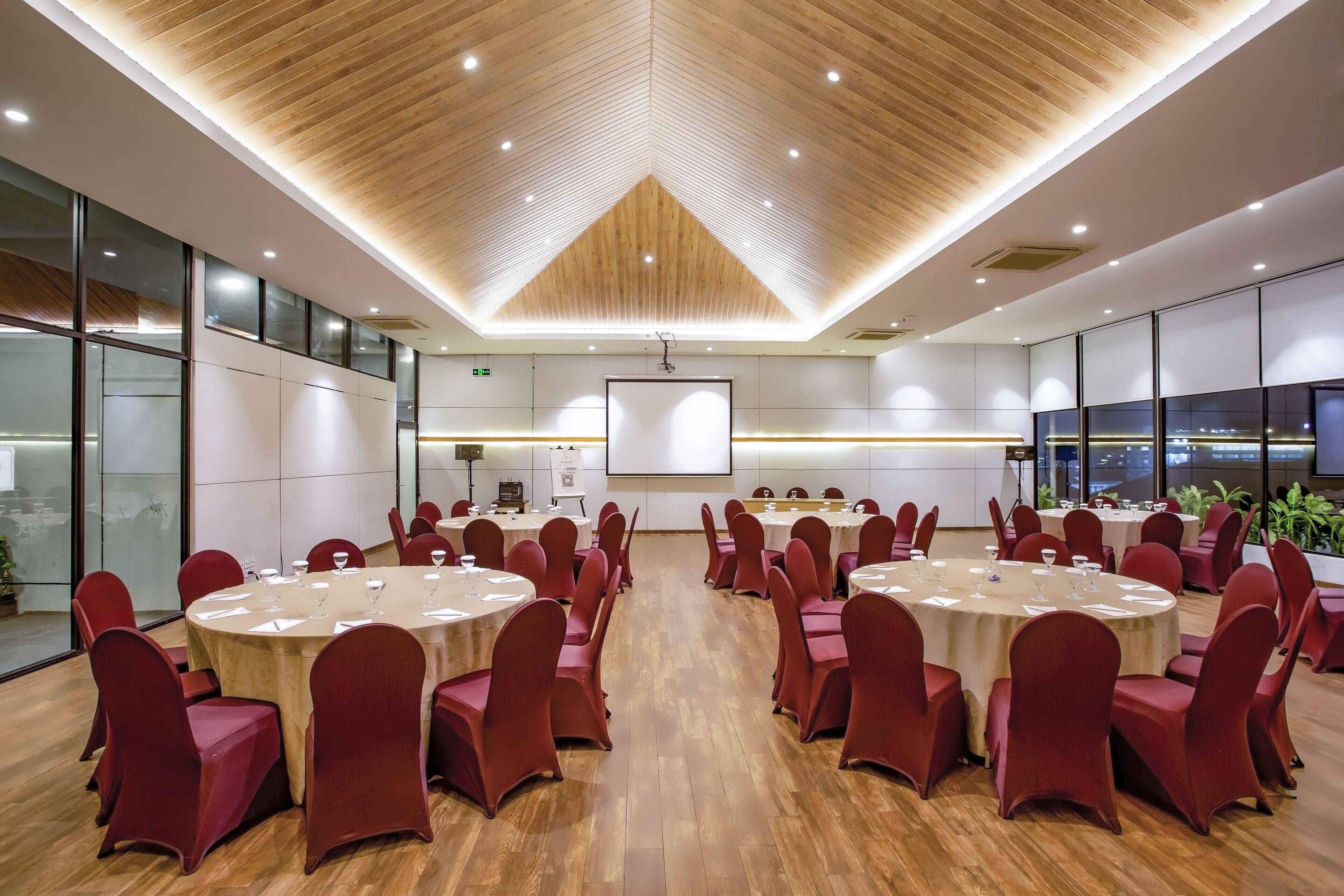 Un salón de conferencias con mesas redondas, sillas rojas y techo de madera.