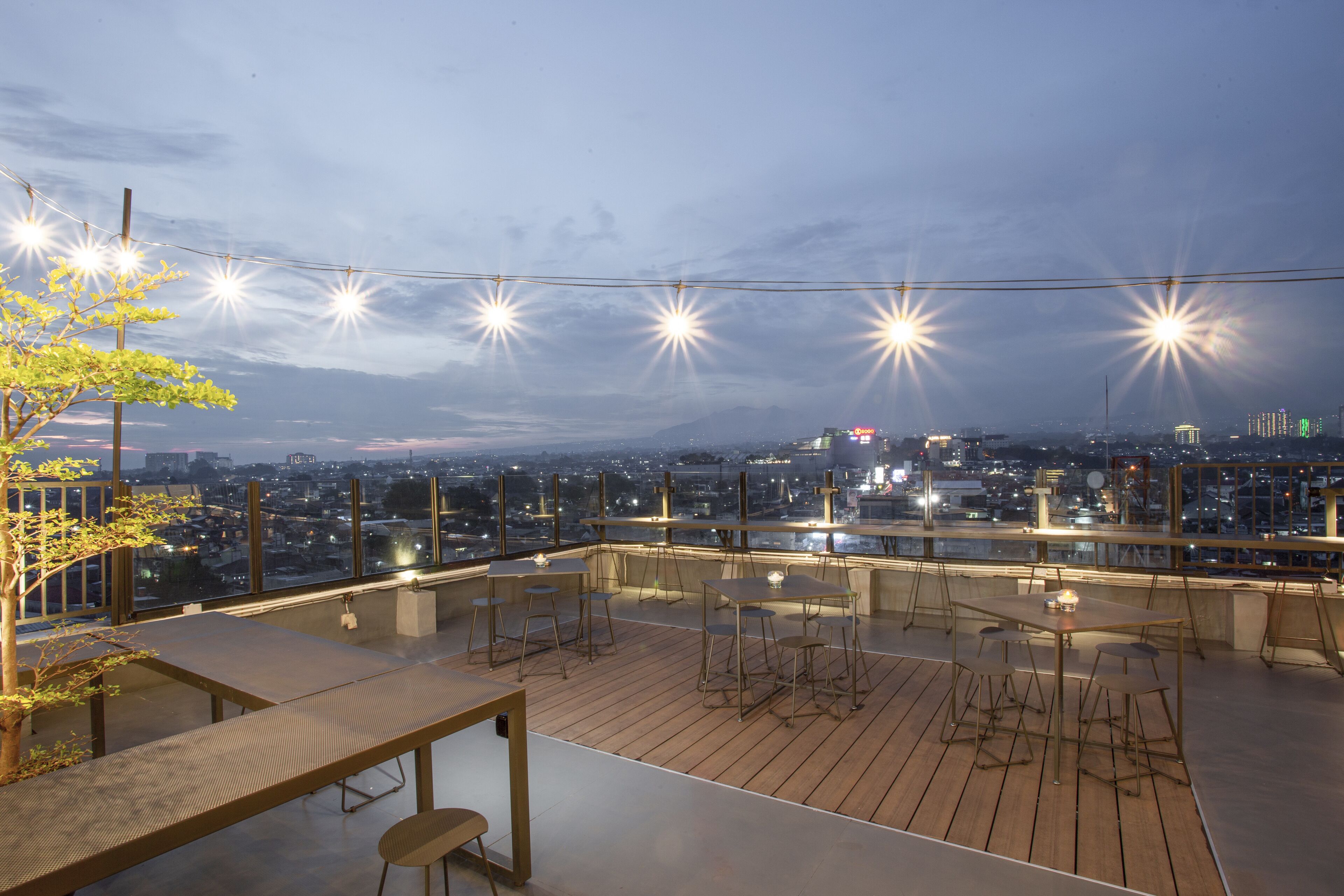 A rooftop terrace with tables and chairs, string lights, and a cityscape view.