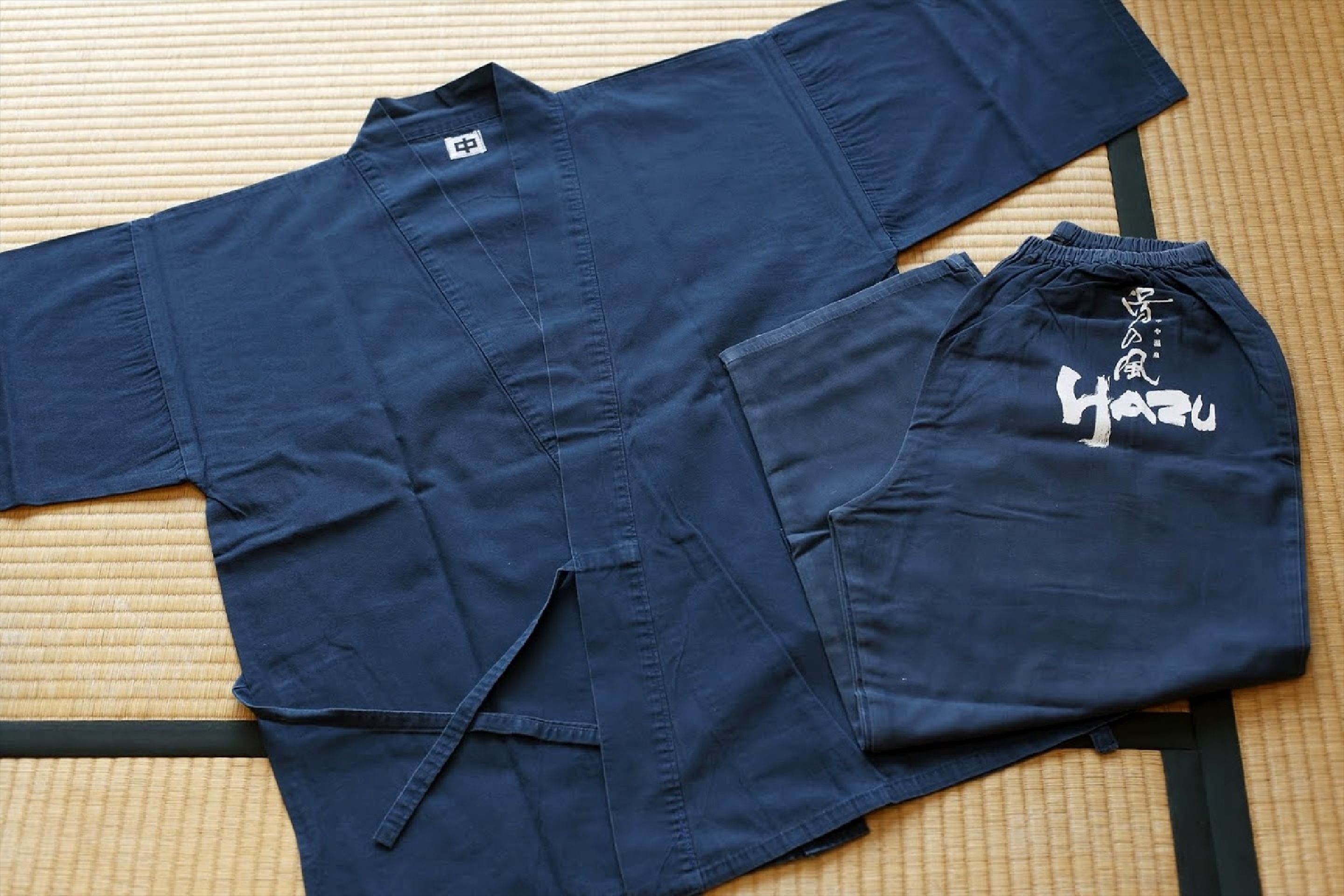 A dark blue martial arts gi laid out on a woven mat.