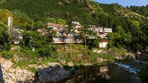 Un edificio de varios pisos con un río al frente, rodeado de abundante vegetación y colinas.