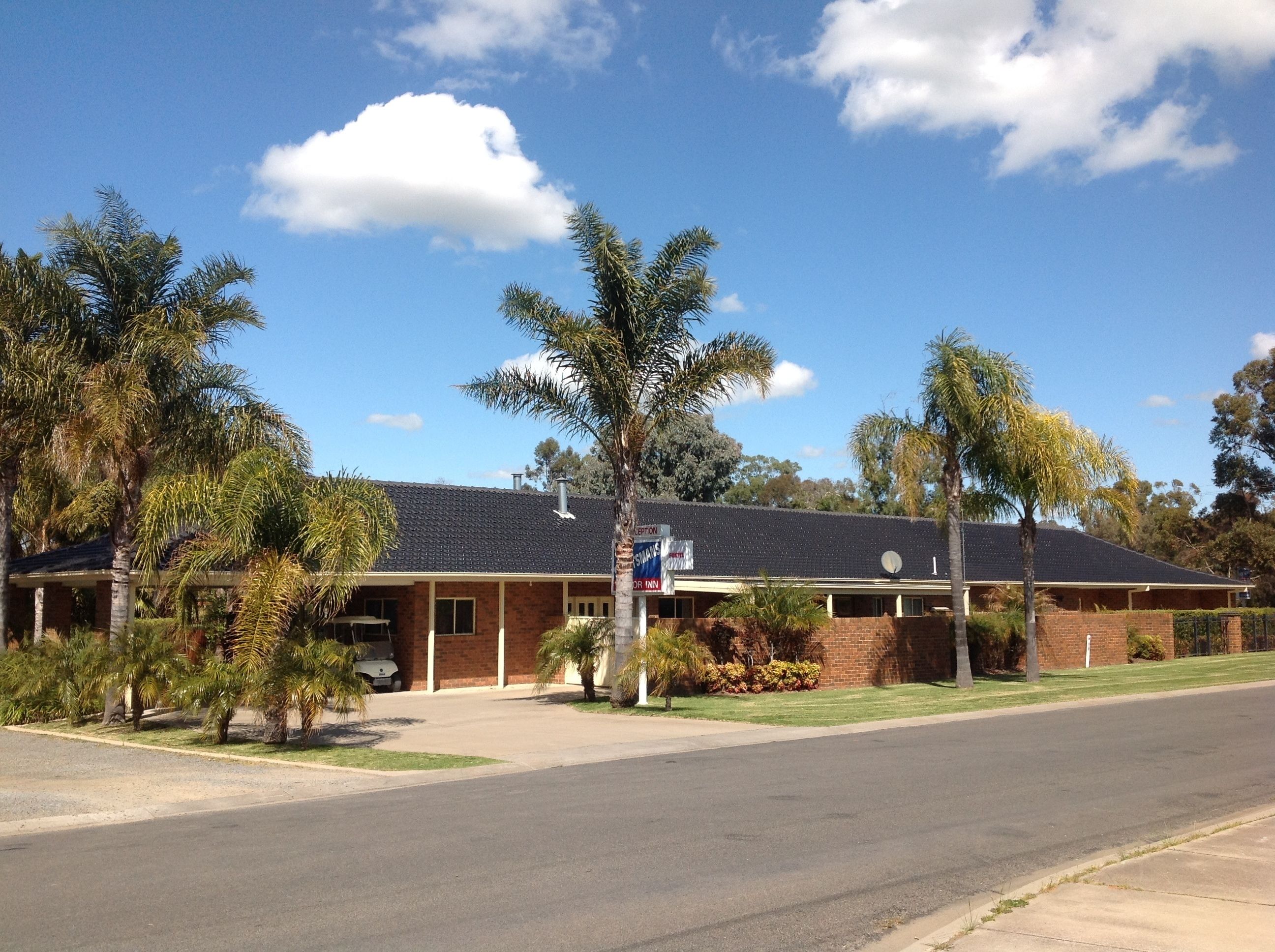 A motel with a brick facade, a covered parking area, and palm trees in the foreground.