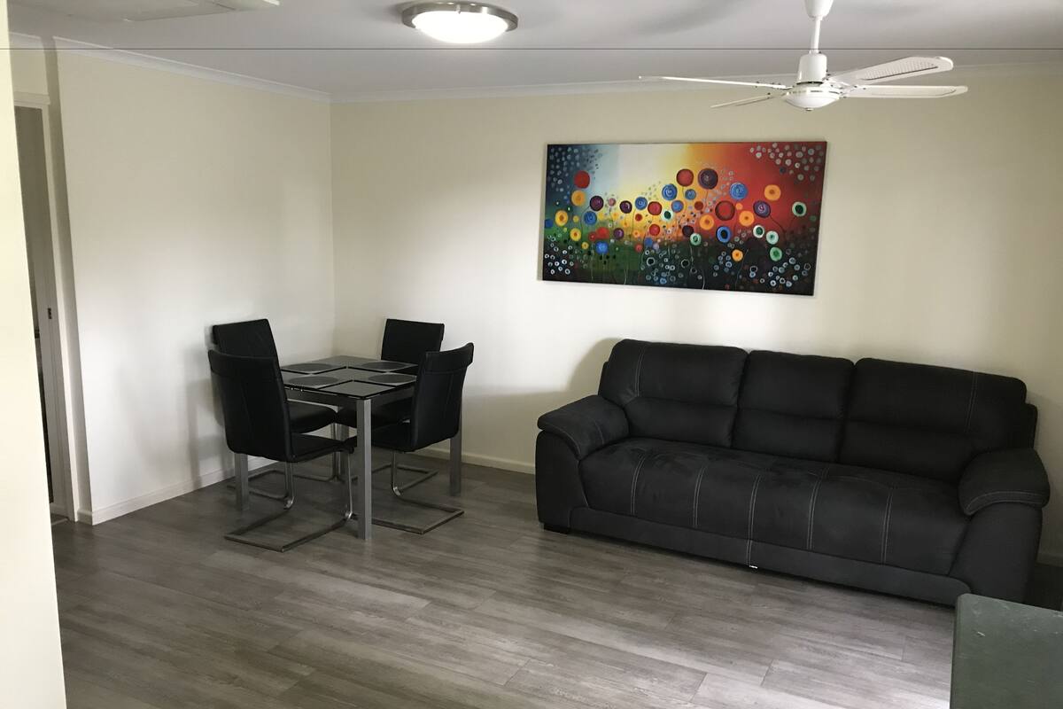 A living room with a black leather sofa, a dining table with four chairs, and a ceiling fan.