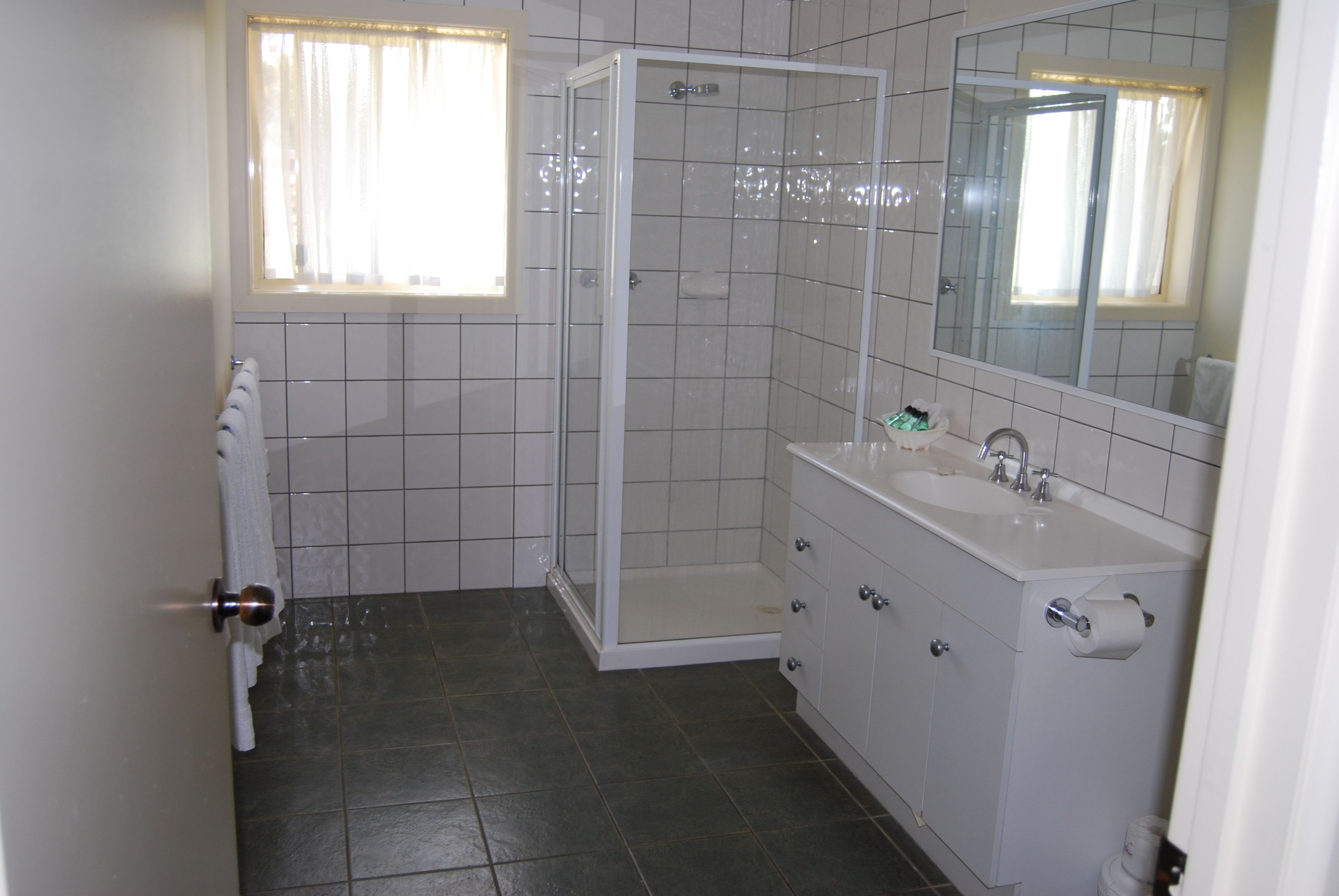 Un baño con ducha, lavabo, espejo y barra para toallas.