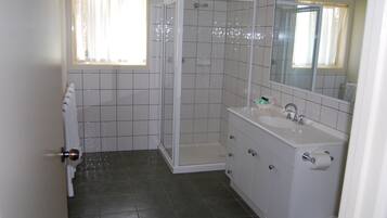Un baño con ducha, lavabo, espejo y barra para toallas.