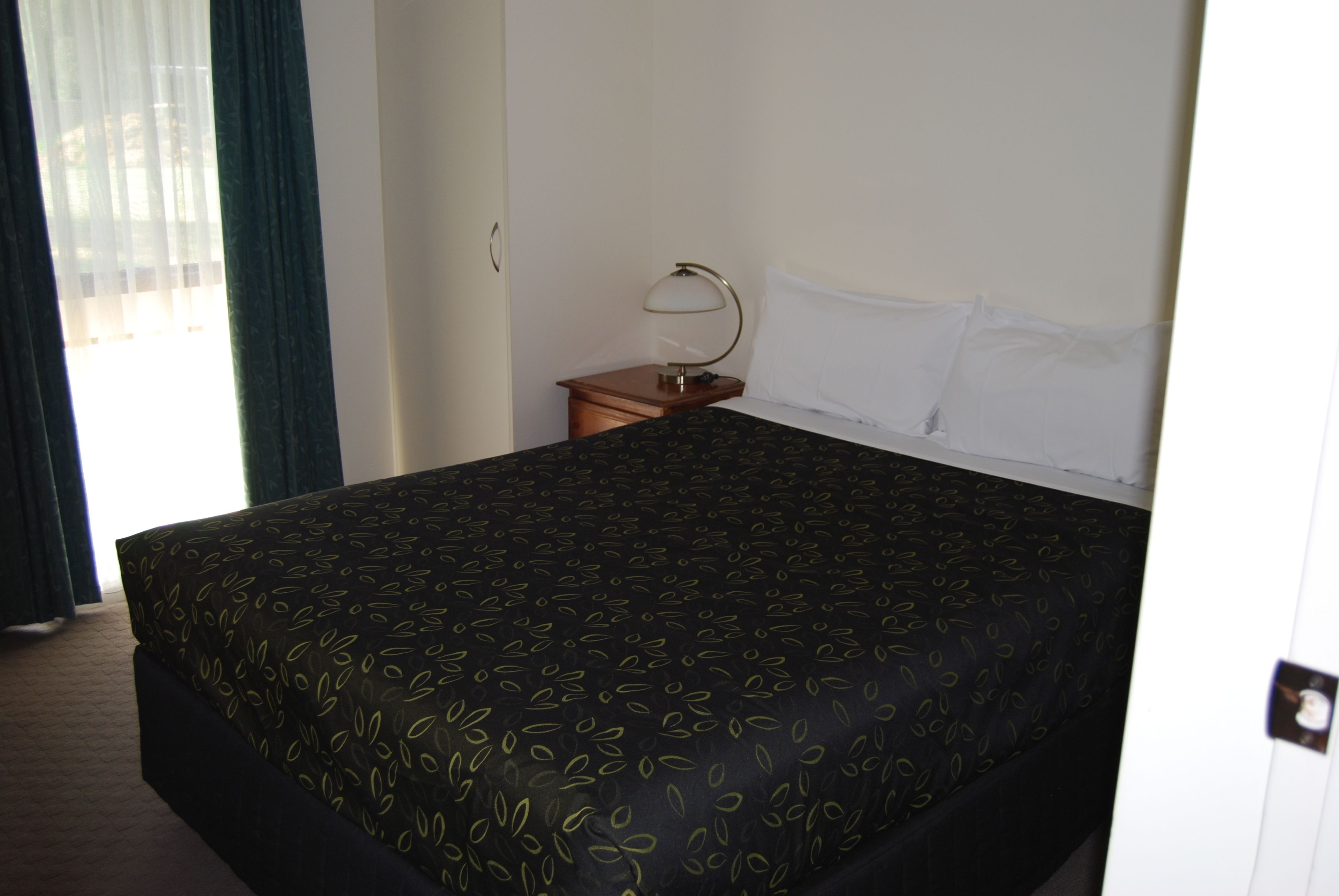 Una camera d'albergo con un letto grande, un comodino con una lampada e una finestra con tende.