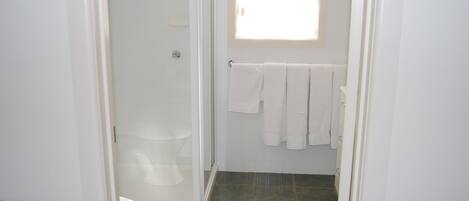 Un baño con cabina de ducha de vidrio, inodoro y toallero con varias toallas.