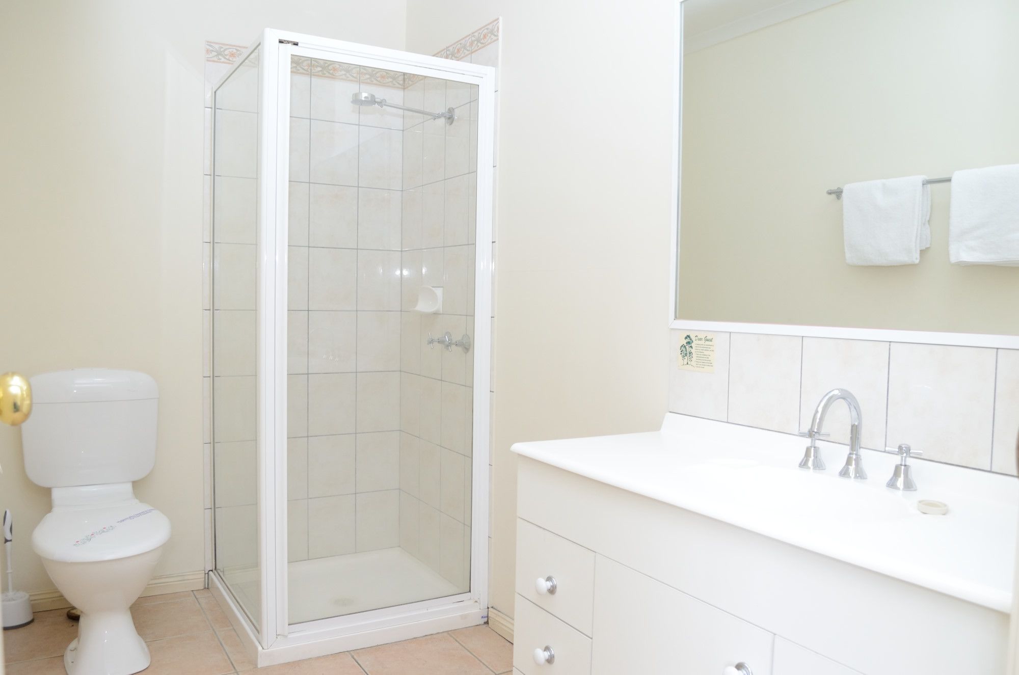 A bathroom with a glass-enclosed shower, a toilet, and a sink with a mirror above it.