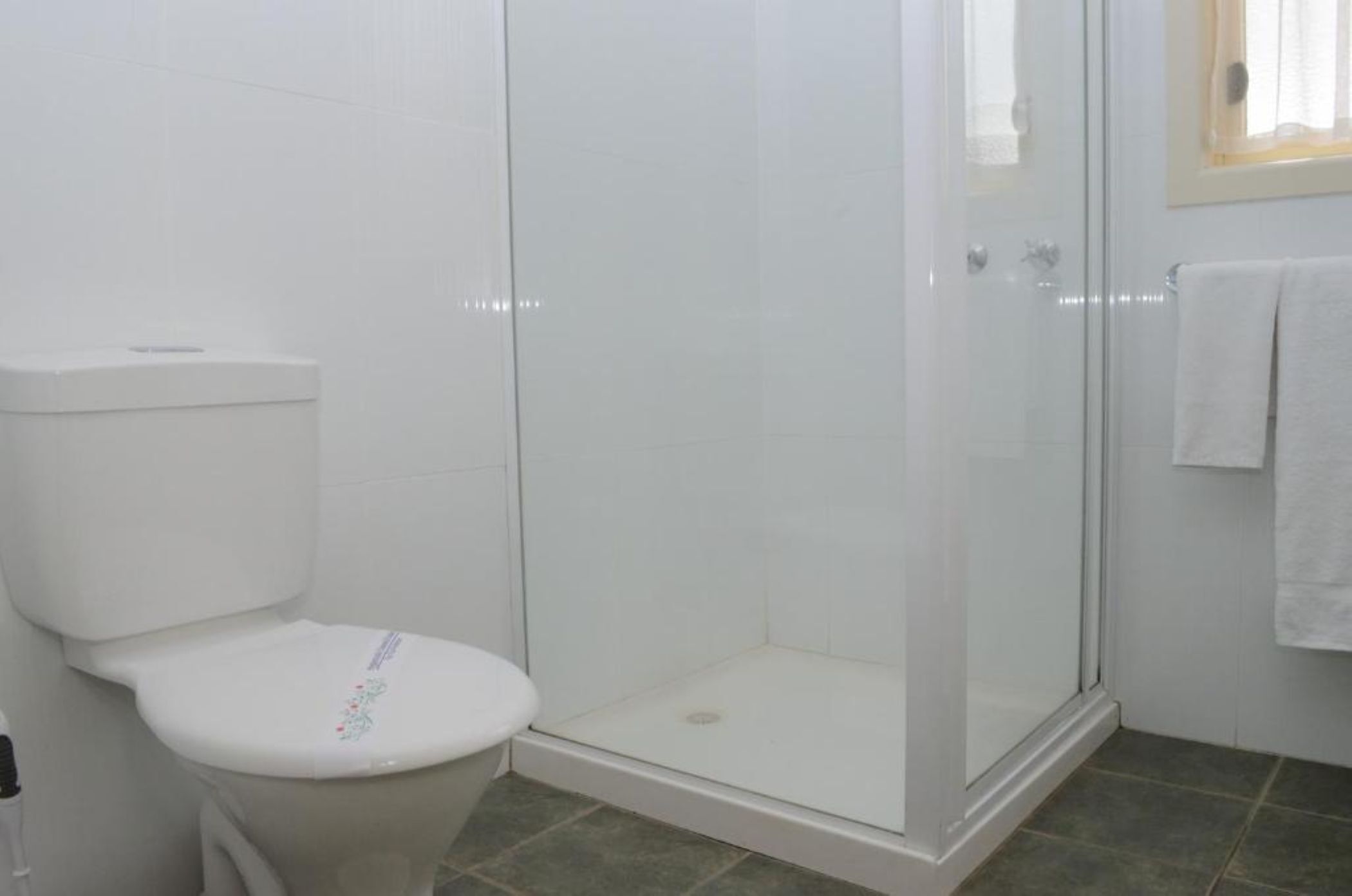 Un baño con inodoro, ducha de vidrio y toalla blanca colgada en la pared.