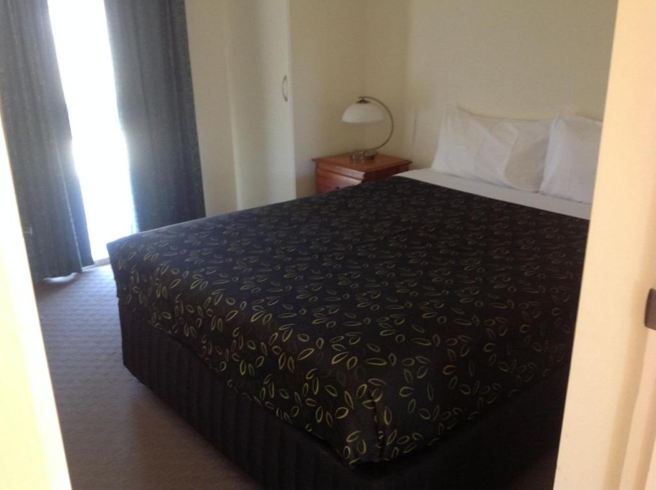 A hotel room with a bed, a nightstand, a lamp, and a window with curtains.