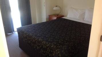 A hotel room with a bed, a nightstand, a lamp, and a window with curtains.