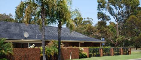A two-story house with a tiled roof, brick exterior, and a small front yard with a palm tree and a fence.