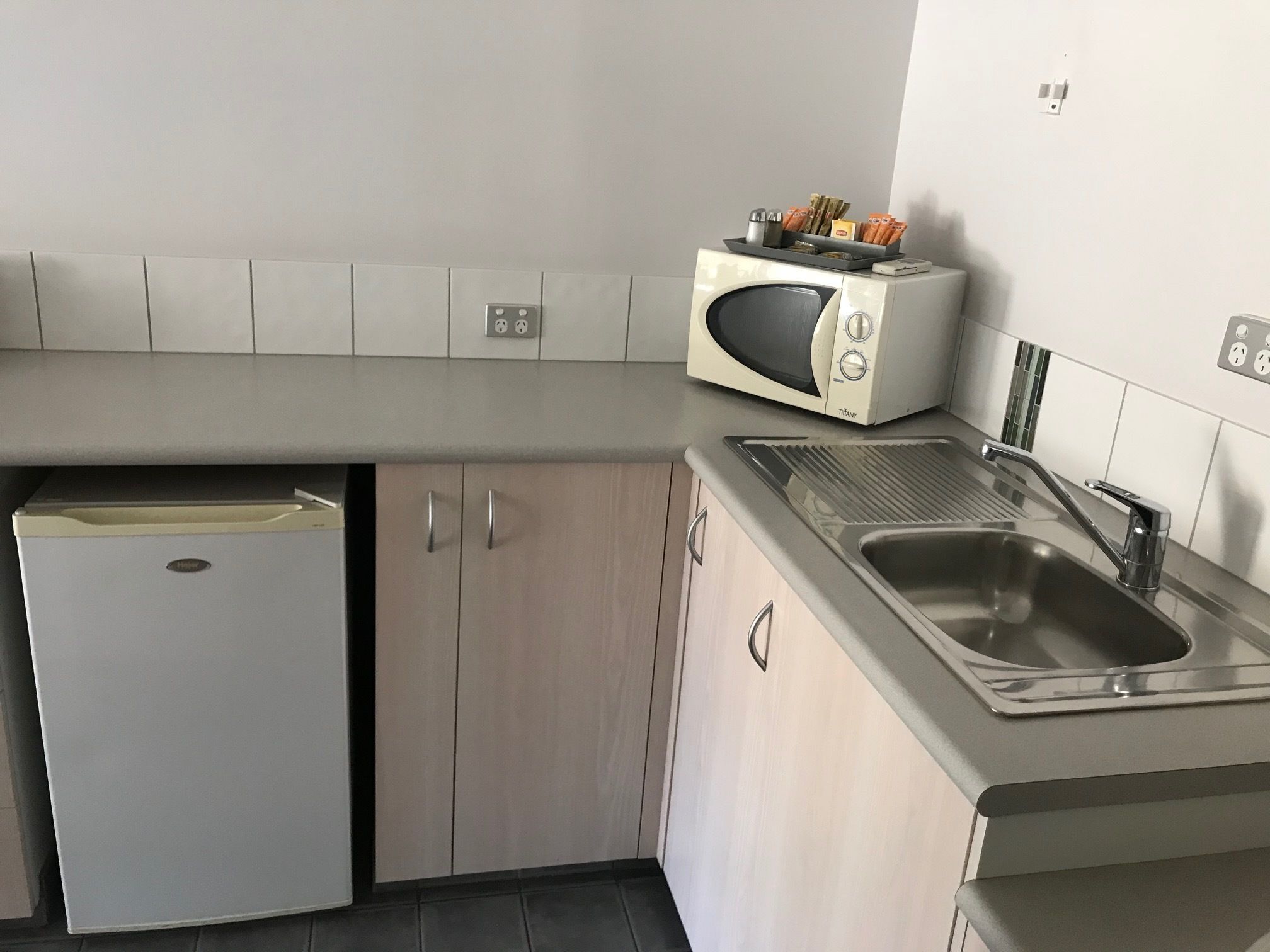Een kleine keuken met een inbouwmagnetron, een spoelbak en een kleine koelkast.