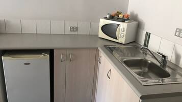 Een kleine keuken met een inbouwmagnetron, een spoelbak en een kleine koelkast.