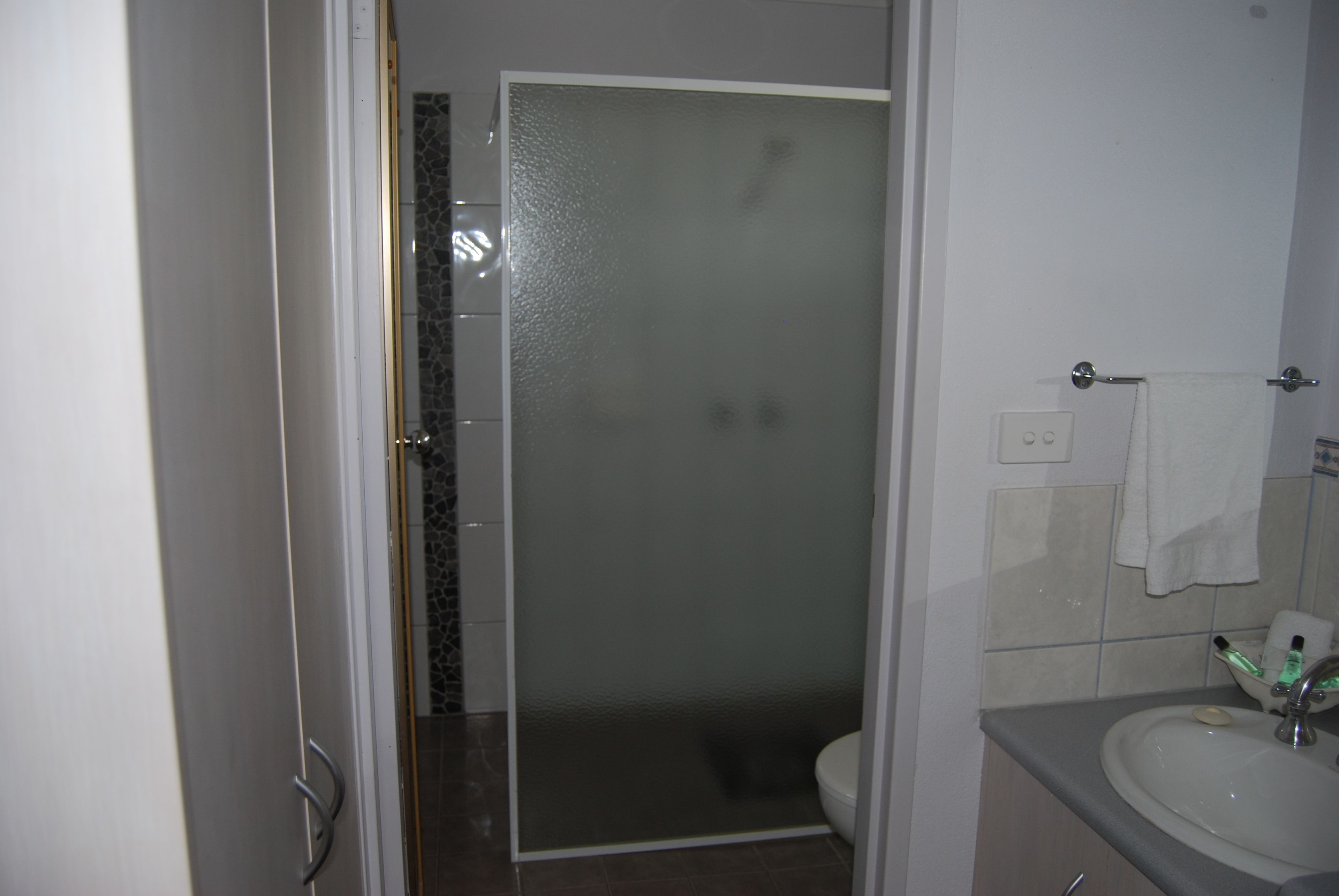 Un bany amb un cubicle de dutxa de vidre, un vàter i un lavabo amb una tovallola penjada a la paret.