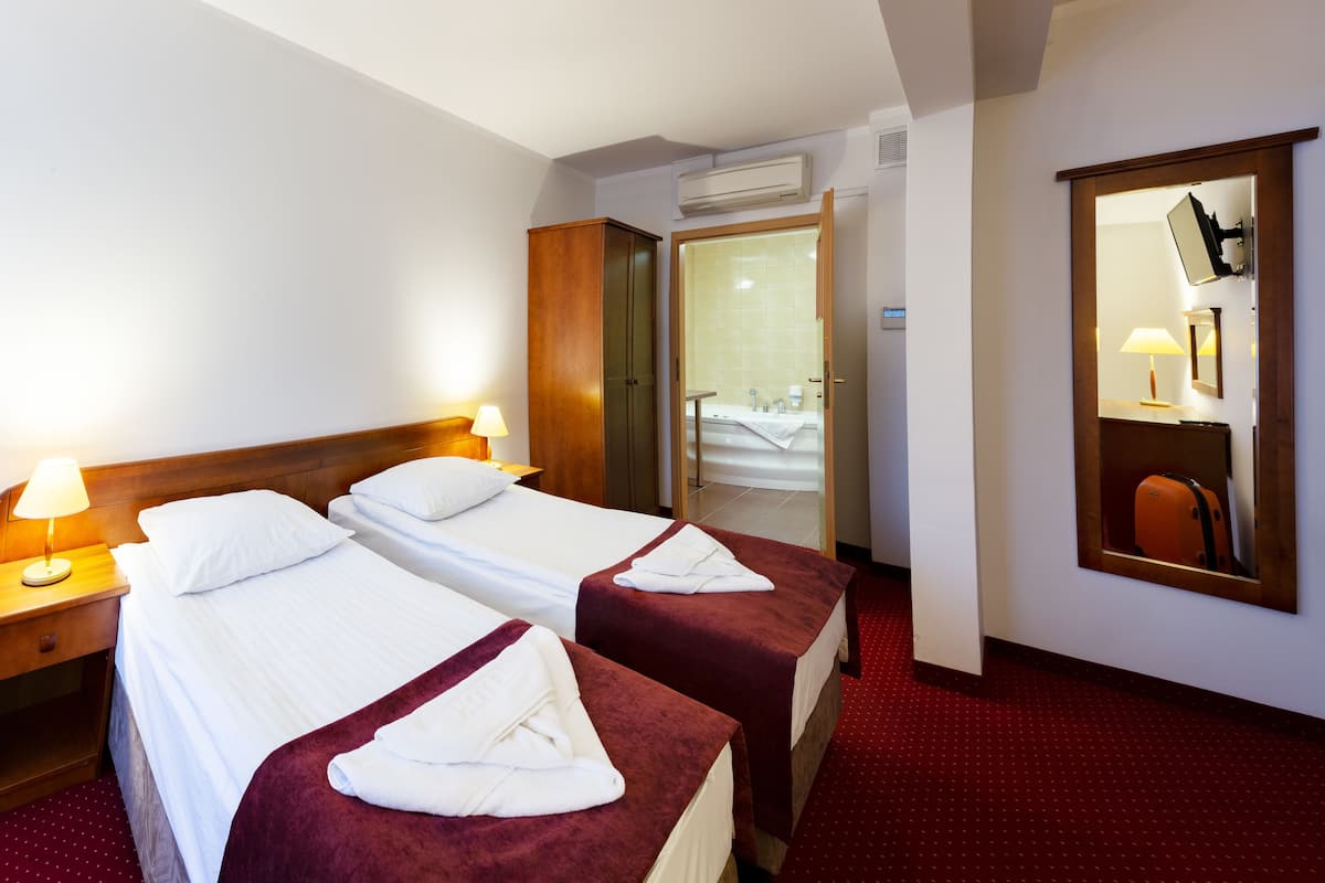Habitació d'hotel amb dos llits, un armari de fusta, un mirall i una catifa vermella.