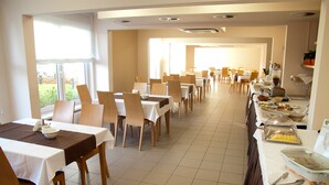 A spacious dining area with multiple tables and chairs, a buffet line with various food items, and large windows providing natural light. - Hotel Zawisza (Bydgoszcz)