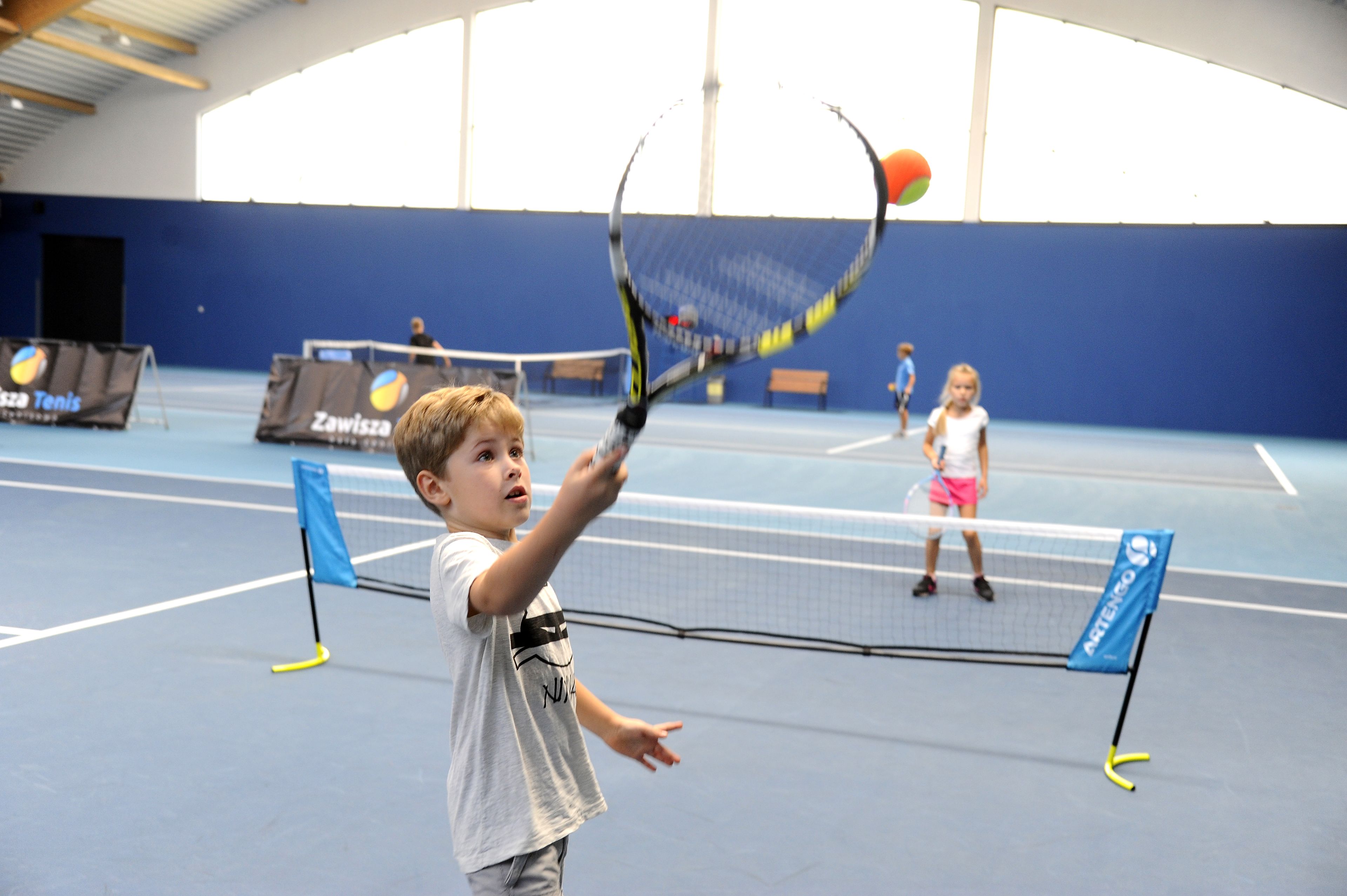 A tennis court with a net, blue walls, and a high ceiling.