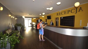 A reception area with a wooden reception desk, a wall-mounted TV, and a sign that reads "RECEPCJA". - Hotel Zawisza (Bydgoszcz)