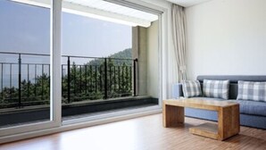 A modern living room with a large window, a blue sofa, and a wooden coffee table. - Lapis Hotel (Namhae)