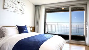 A hotel room with a large bed, a view of the sea through a sliding glass door, and a painting on the wall. - Lapis Hotel (Namhae)