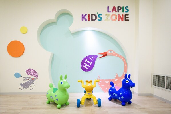 A children's play area with a large wall decoration, three toy animals, and a wall sign reading "LAPIS KIDS ZONE".