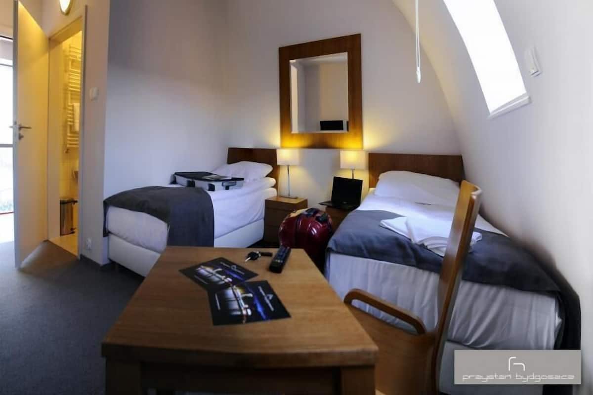 Une chambre d’hôtel avec deux lits, une table en bois, un miroir et un petit bureau avec une lampe.