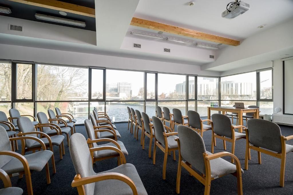 A conference room with rows of chairs facing a large window overlooking a body of water and buildings.