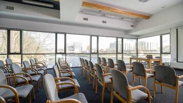 Un salón de conferencias con filas de sillas orientadas hacia un ventanal con vistas a un cuerpo de agua y edificios.