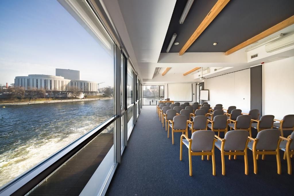 A conference room with a view of a river and buildings, arranged with rows of chairs.