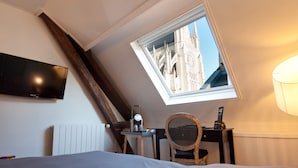 A bedroom with a sloped ceiling, a skylight, a bed, a desk, a chair, and a television. - Hôtel le Prieuré (Amiens)