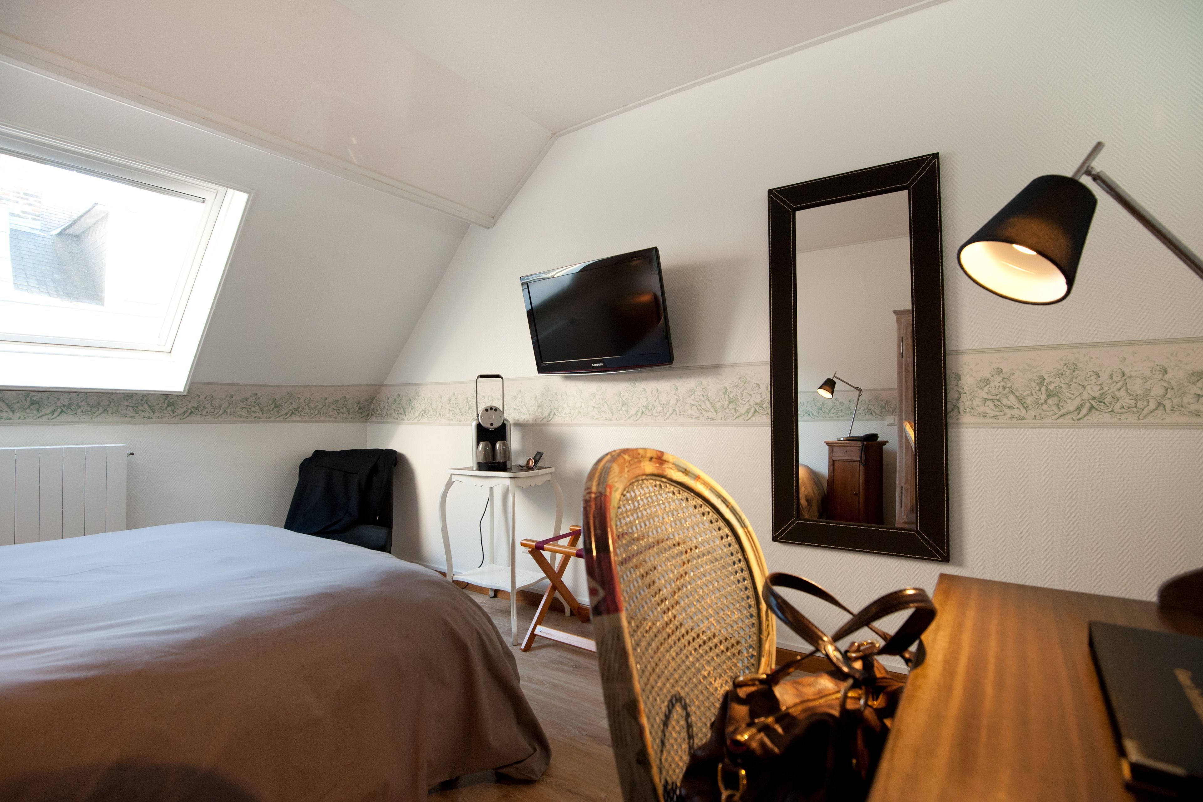 A hotel room with a bed, a desk, a chair, a television mounted on the wall, and a window.