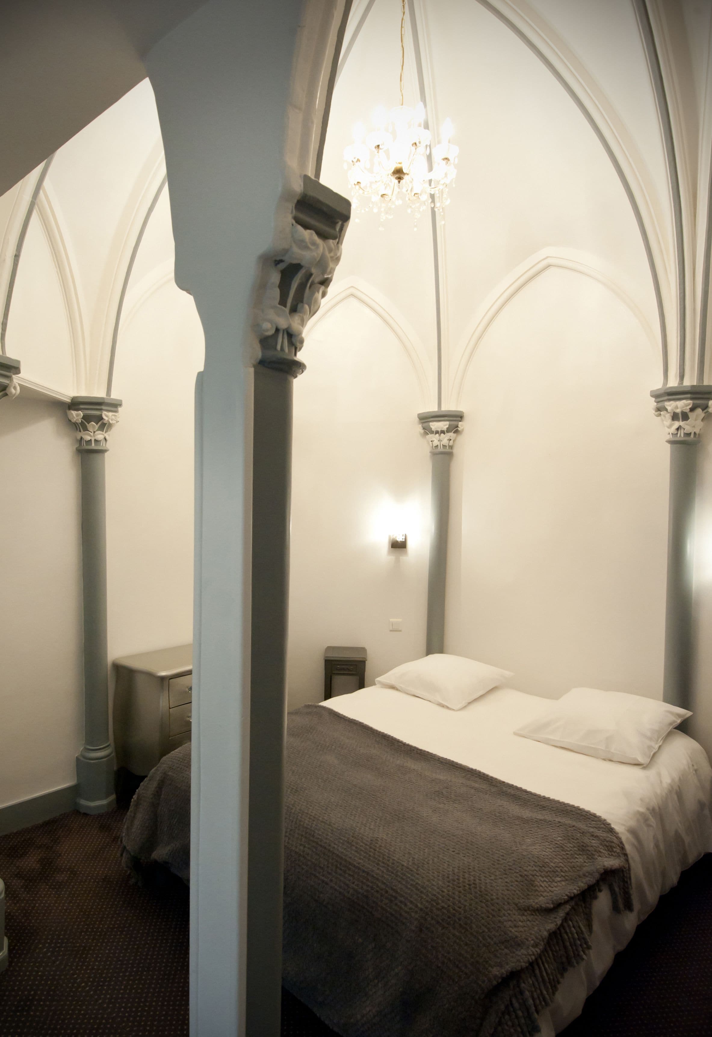 A bedroom with a bed, a chandelier, and Gothic-style columns.