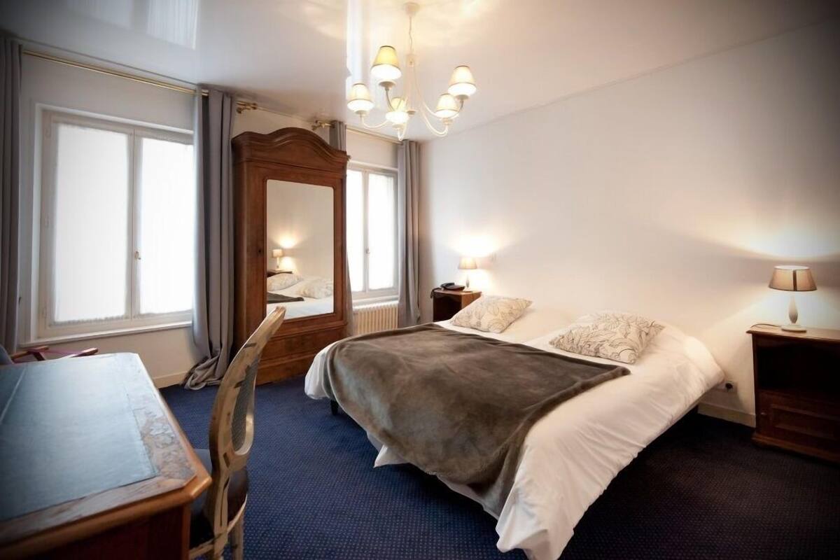 A hotel room with a bed, a desk, a chair, a mirror, and a chandelier.