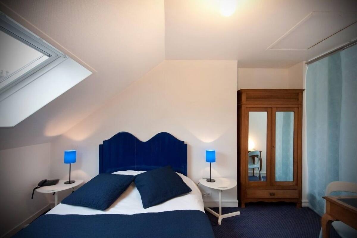 A hotel room with a bed, two bedside tables with lamps, a wardrobe, and a door.