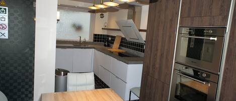 A modern kitchen with a wooden table, stainless steel appliances, and a black and white tiled backsplash.