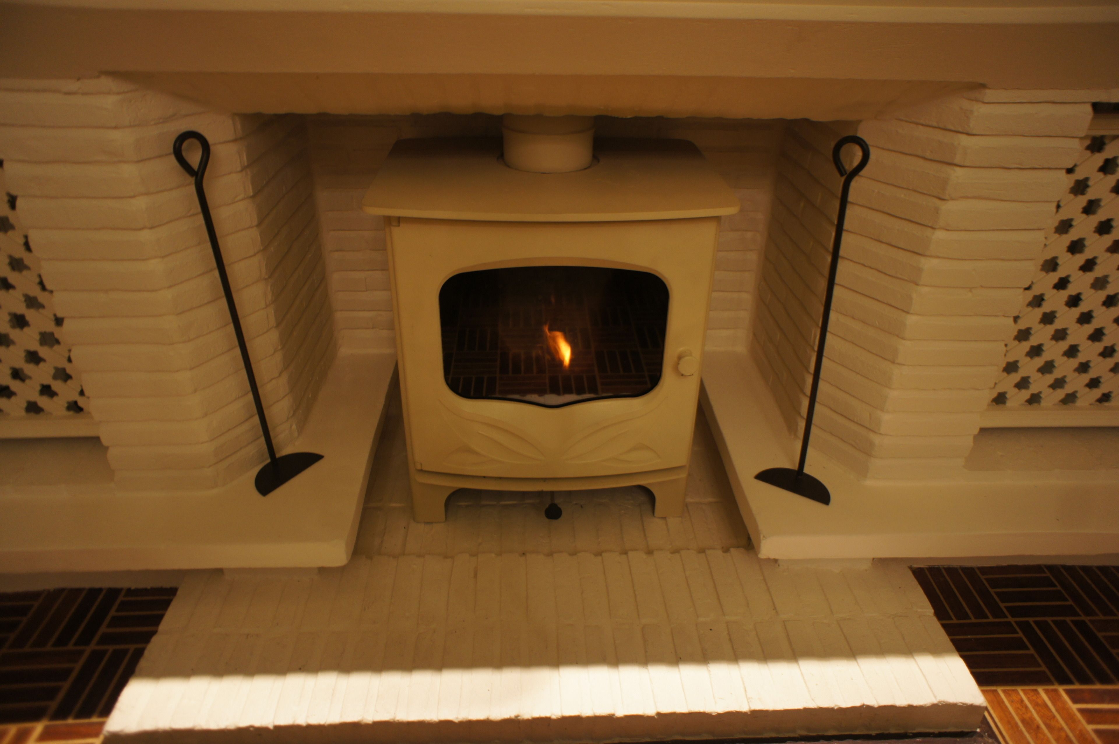 Una estufa de leña blanca con fuego visible, flanqueada por paredes de ladrillo decorado y un hogar blanco.