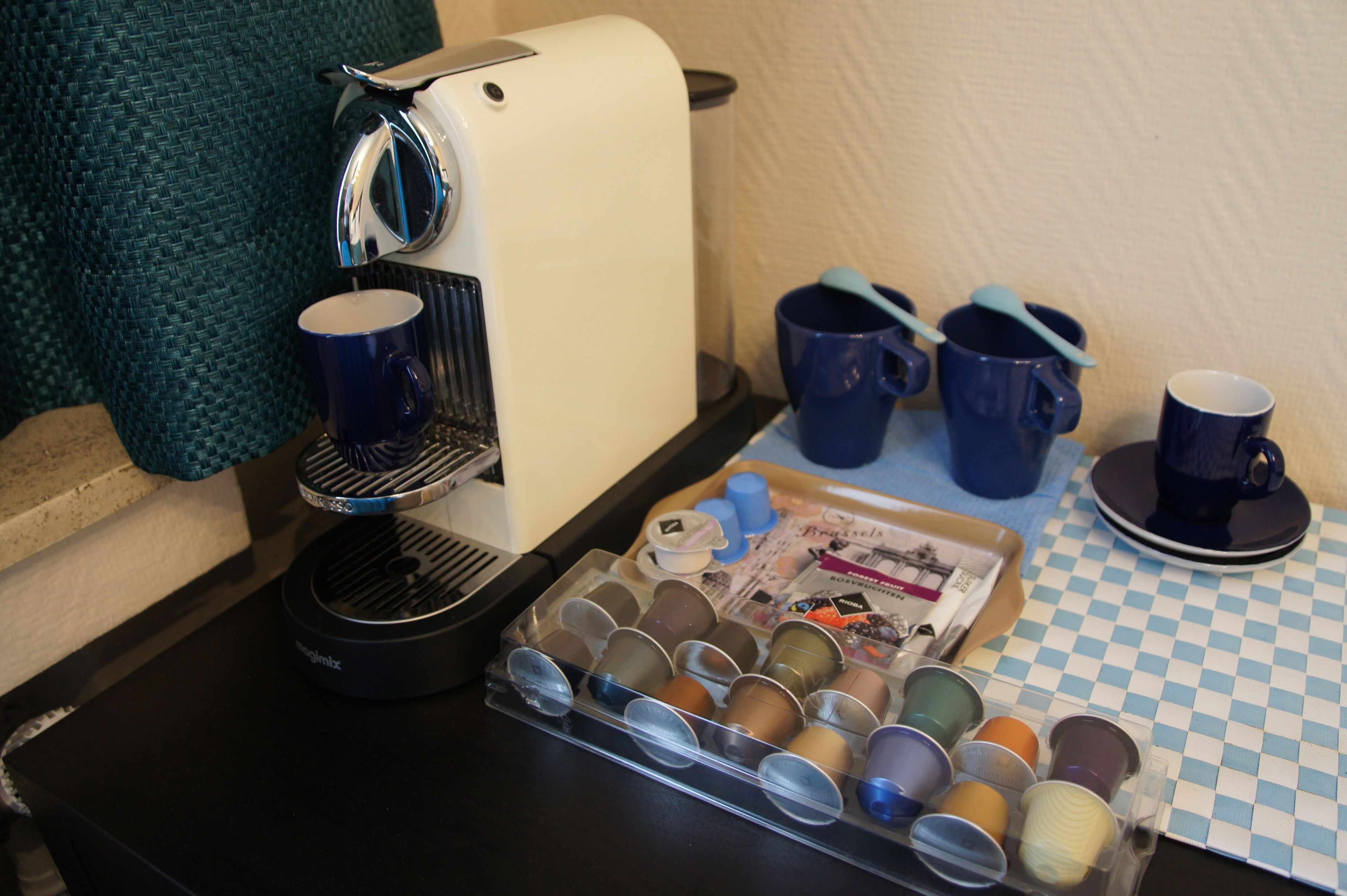 A coffee maker, a tray of coffee cups, and a checkered tablecloth.