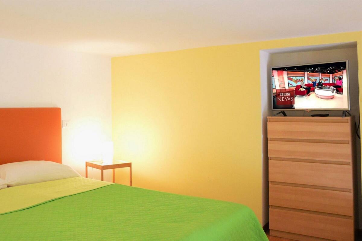 Ein Hotelzimmer mit einem Bett, einem kleinen Tisch und einem Fernseher, der einen Nachrichtensender zeigt.