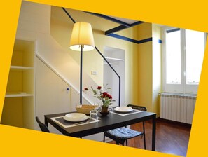 Un coin repas avec une table dressée pour deux personnes, une lampe et un vase rempli de fleurs.