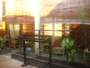 A room with bamboo blinds, wicker furniture, and potted plants. - Syifa Homestay (Gili Trawangan)