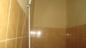 Een hoek van een badkamer met een douchekop aan een wand, betegeld in een lichtbruine kleur.